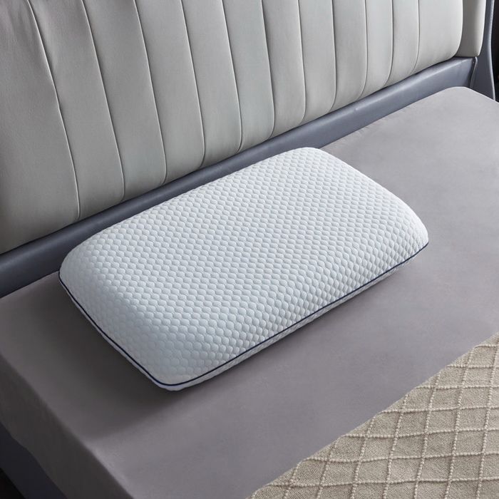 A memory foam pillow with a textured cover resting on a bed with a quilted mattress
