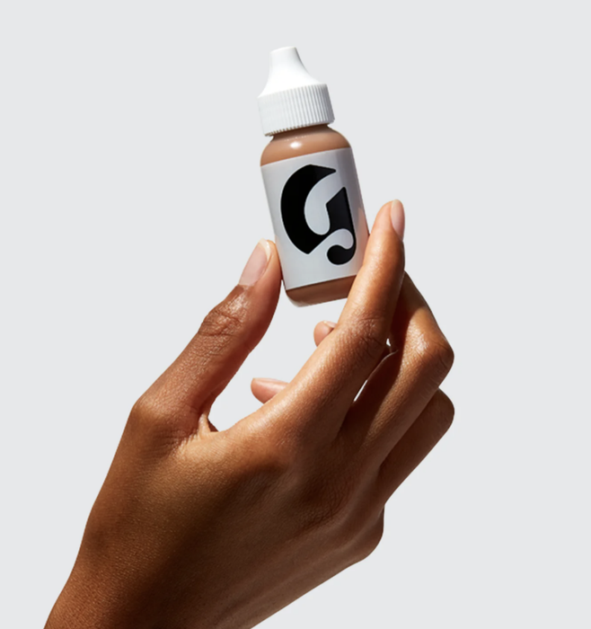 Model holding a bottle of Glossier Perfecting Skin Tint