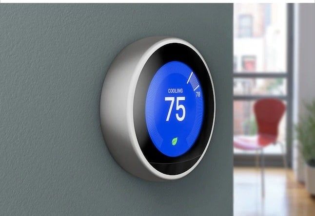 a black smart thermostat mounted on a green wall