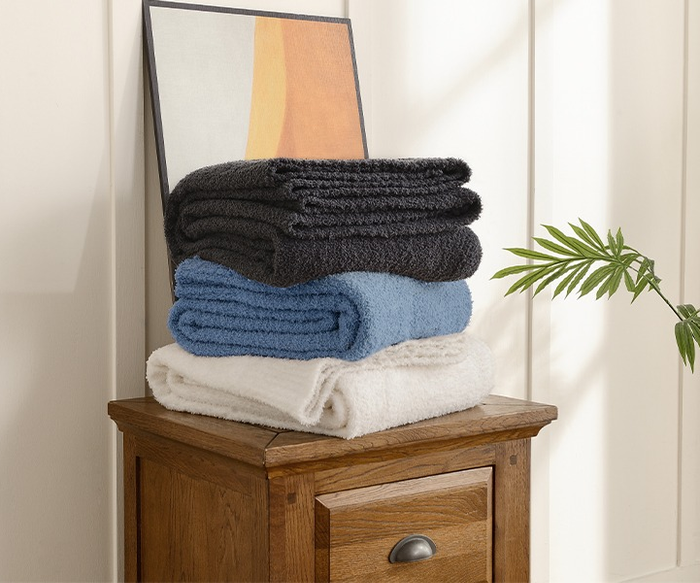 Three neatly folded blankets in shades of dark gray, light blue, and white are stacked on a wooden cabinet, ready for use.