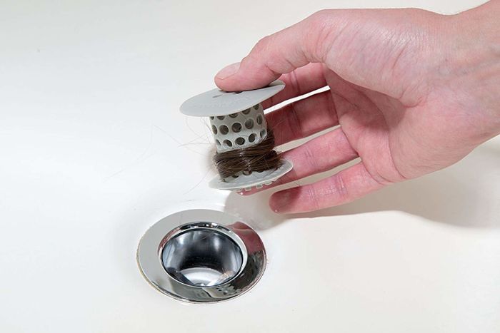 A person is removing the TubShroom from their drain, showing how it keeps the pipes clear of hair buildup.