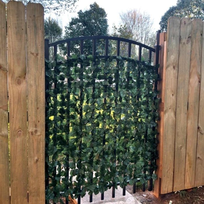 An iron gate with a privacy screen made of artificial green leaves, framed by wooden fence panels.