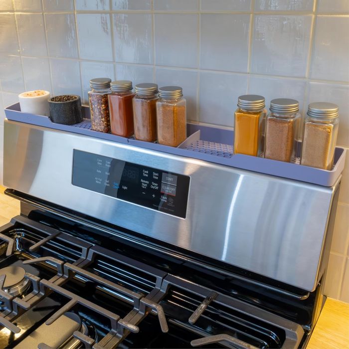 A kitchen stove topped with a silicone magnetic shelf, showcasing various spice jars and a small potted plant, creating a neat and efficient cooking environment.