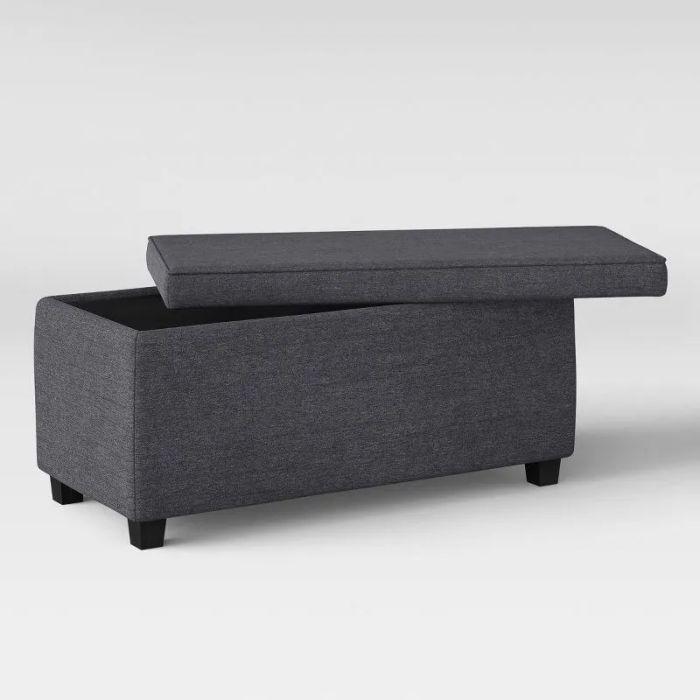 A dark fabric upholstered storage ottoman with a raised lid revealing an interior compartment