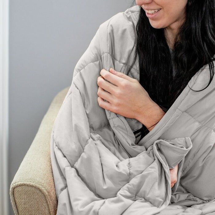 A person sitting on a couch, wrapped in a quilted blanket, smiling contentedly