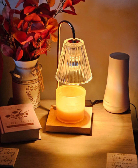 A cozy table arrangement with a lamp, a candle, autumn leaves in a vase, and two books, creating a warm and inviting vibe.