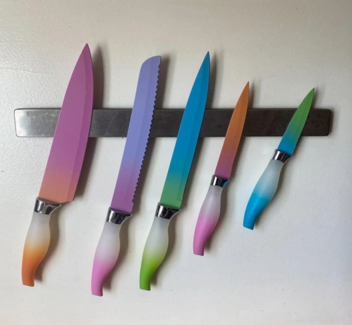 Five kitchen knives with colorful handles and blades, displayed on a magnetic strip