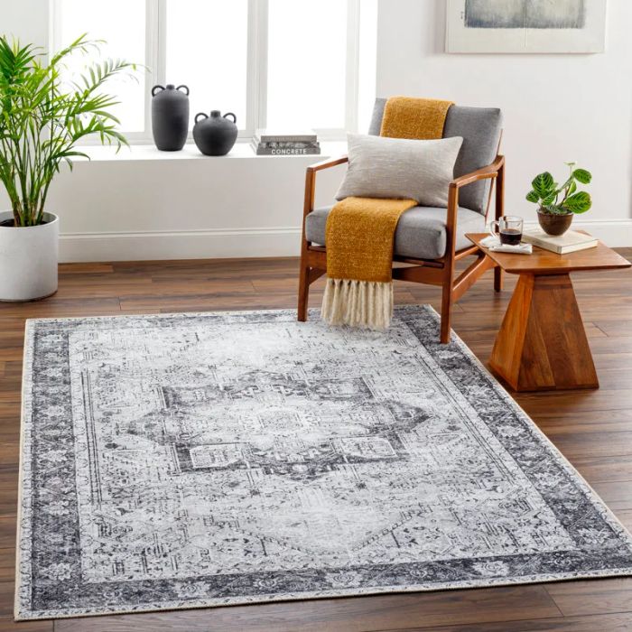 A chic living room featuring a patterned rug, a fringed blanket draped over an armchair, a wooden side table with a plant, and another potted plant near the window.