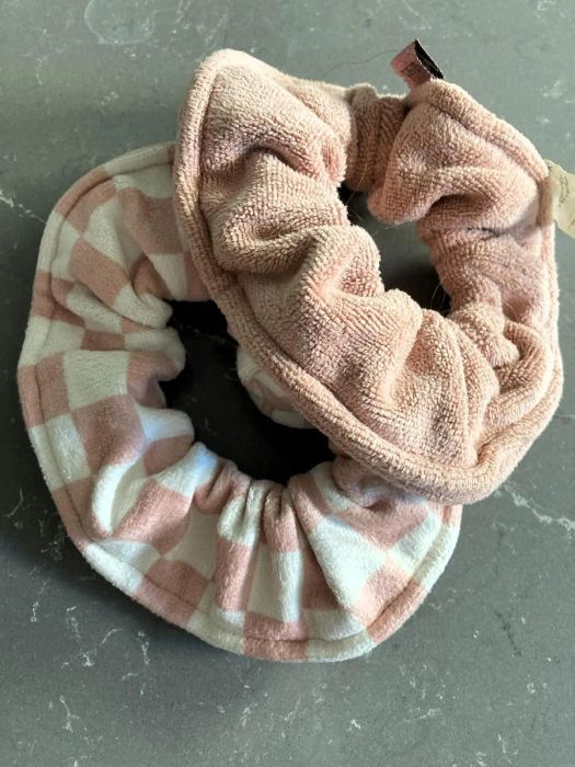Two textured hair scrunchies, one with a checkered pattern and the other a solid color, laid out on a flat surface