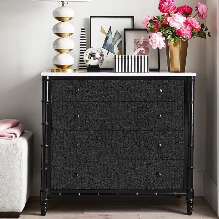 A sleek, black, textured dresser with four drawers, topped with a lamp, framed pictures, a decorative orb, and a vase filled with pink flowers.