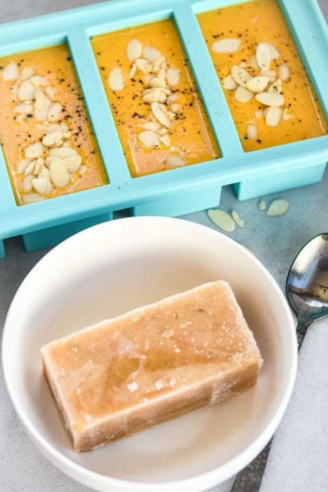 The silicone tray filled with soup, placed next to a bowl containing one of the frozen cubes
