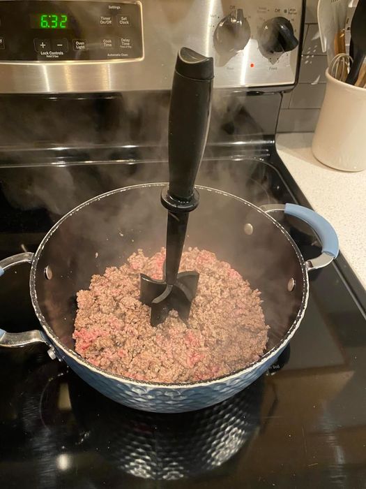 reviewer's beef cooking in a pot with the heat-resistant masher placed in the center