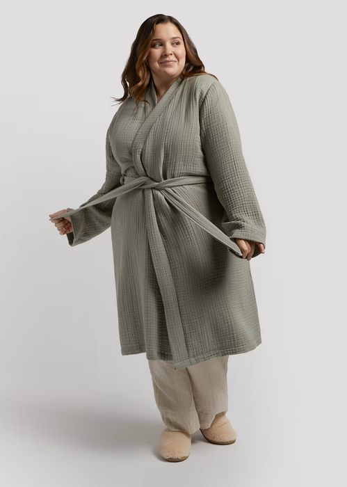 A person dressed in a waffle-textured robe with a tied belt, lounge pants, and slippers, posing comfortably.