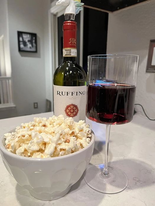 A reviewer's wine bottle, a glass of red wine, and a bowl of popcorn resting on a counter