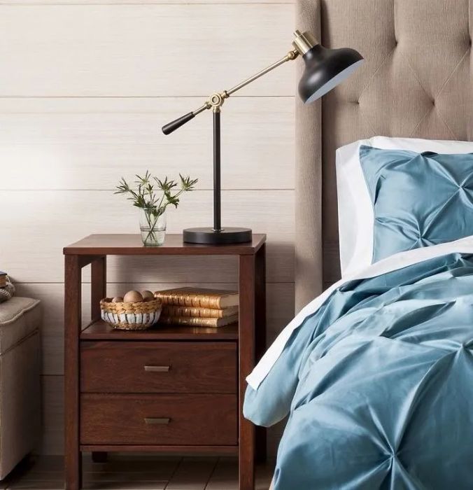 A bedside table with a lamp, decorative plant, and bowls, positioned next to a bed with blue bedding. Perfect for sparking bedroom decor ideas.