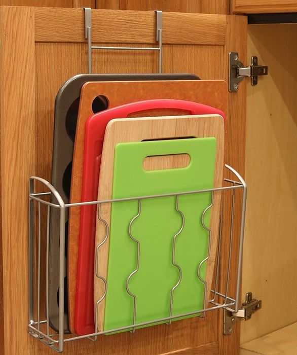 A basket designed to hold a cutting board, conveniently hooked onto the inside of a cabinet for easy access.