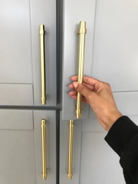 A reviewer installing a shiny gold pull on a kitchen cabinet, adding a stylish upgrade.