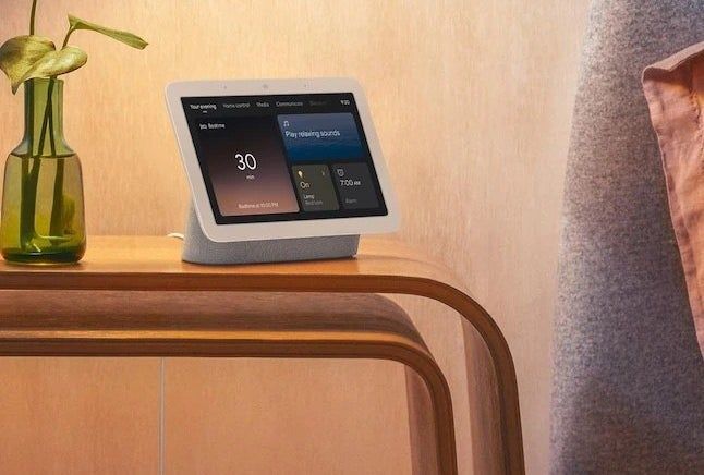 a sleek white smart home speaker placed on a nightstand