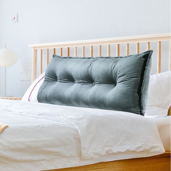 A large, tufted pillow resting against a wooden headboard on a neatly made bed, enhancing the warm and inviting atmosphere of the cozy bedroom setup.