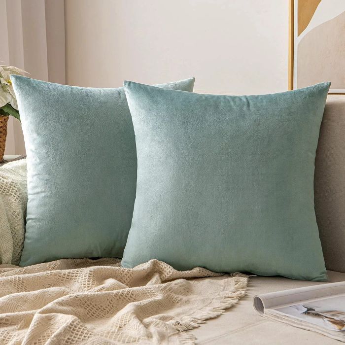 Two blue-grey velvet square throw pillows on a couch.