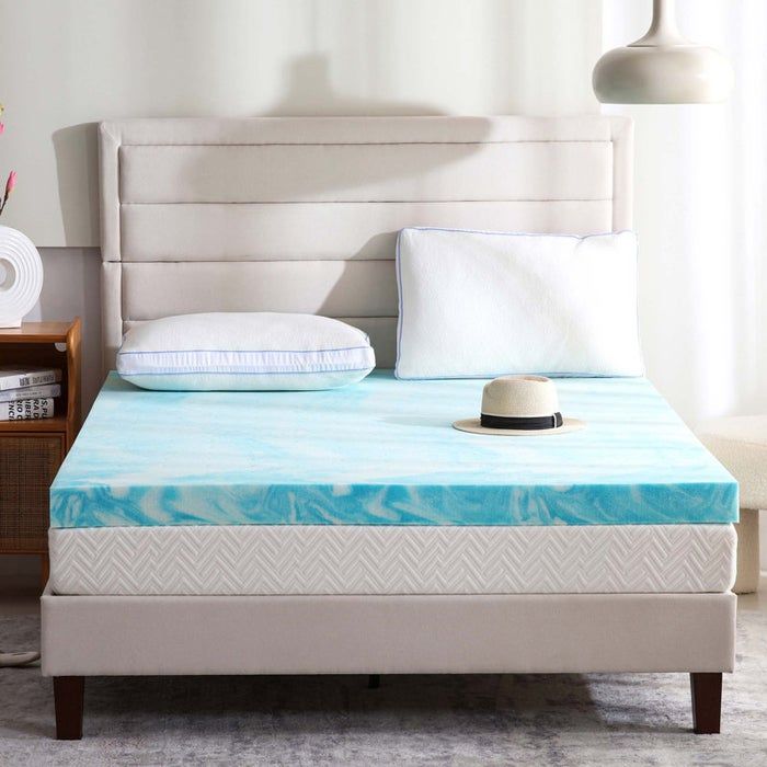 A modern bedroom featuring a bed with a memory foam mattress topper, two pillows, and a hat casually placed on one pillow.