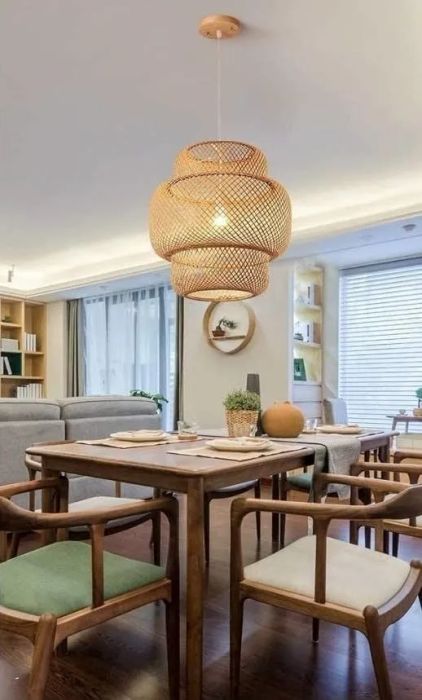 A modern dining room featuring a wooden table, green and white cushioned chairs, and a wicker pendant lamp, with shelves and a window in the background creating a warm atmosphere.