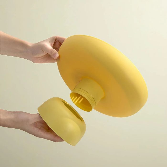 Hands putting together a modern yellow lamp with a round base, demonstrating how its parts come apart for easy assembly.