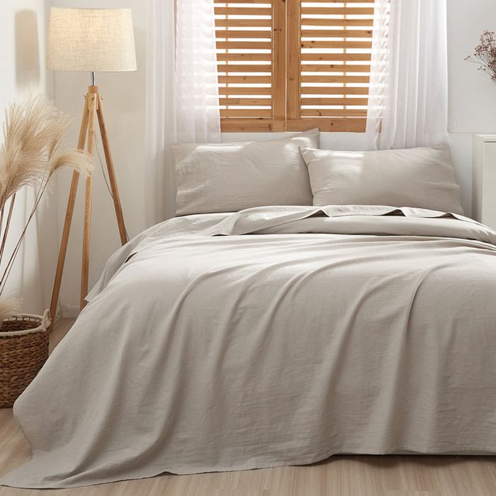 A cozy bedroom featuring a neatly made bed with large pillows, a standing lamp, and decorative plants placed in a basket, creating a warm and inviting atmosphere.