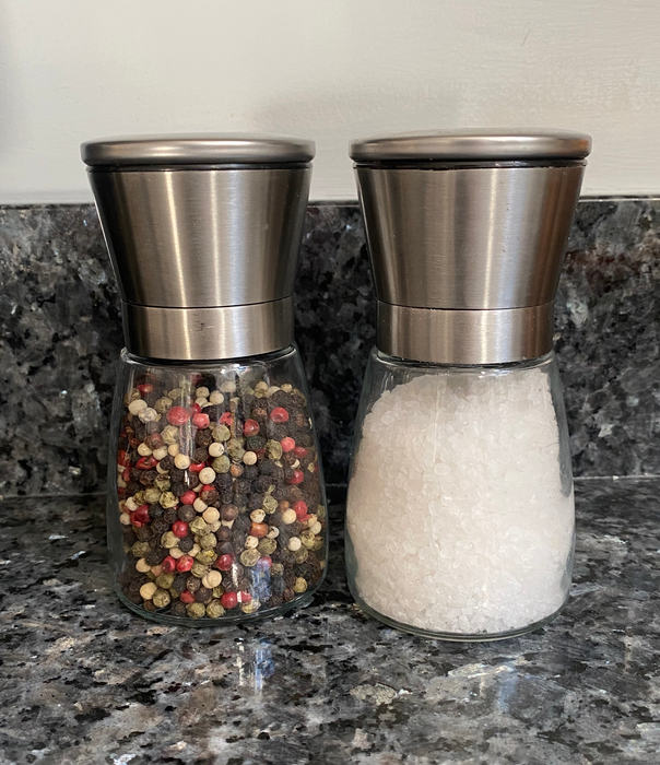 Two glass grinders, with stainless steel tops, filled with pepper and sea salt