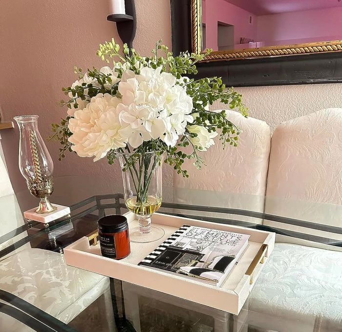 A reviewer's white tray with gold handles, holding a vase of flowers and various other items.