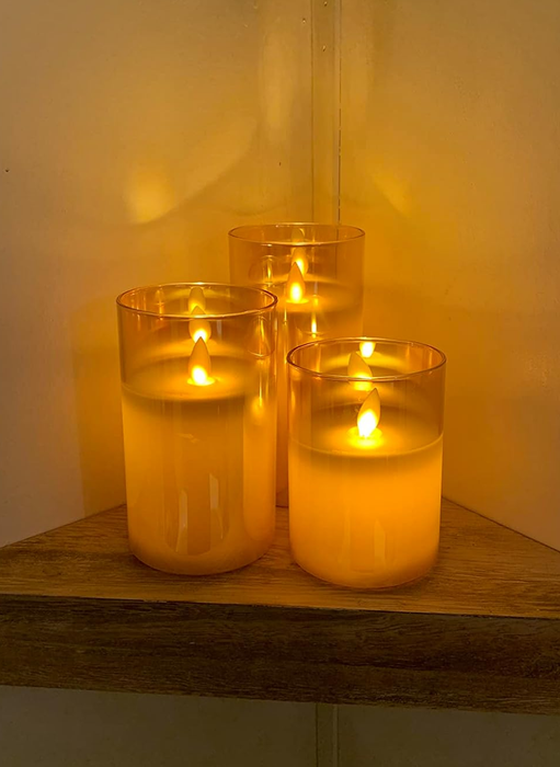 A set of three flameless candles housed in clear glass cylinders.