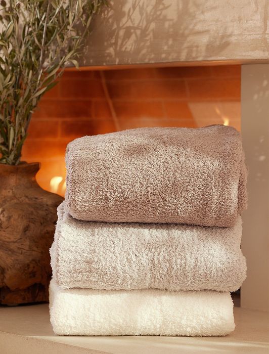 Three soft towels neatly stacked in front of a fireplace, promoting the essence of cozy home goods.