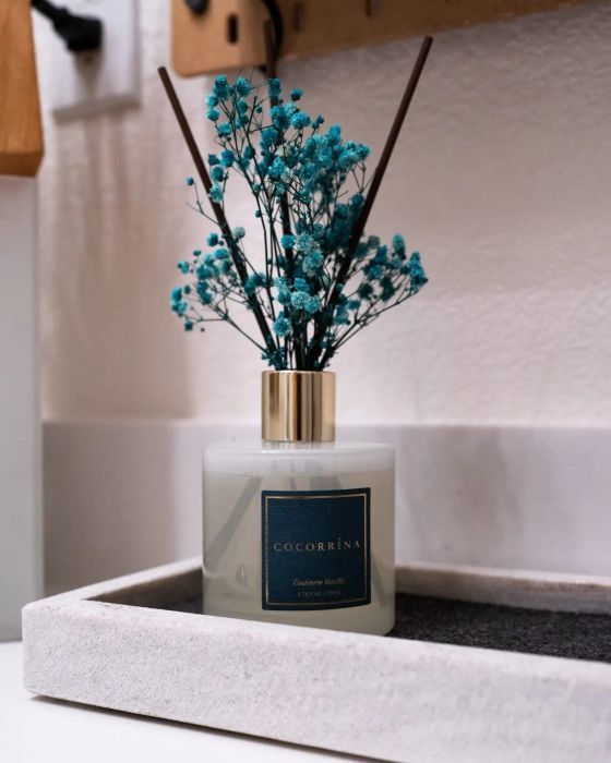 Reviewer's reed diffuser in a square bottle with turquoise flowers displayed on a tray