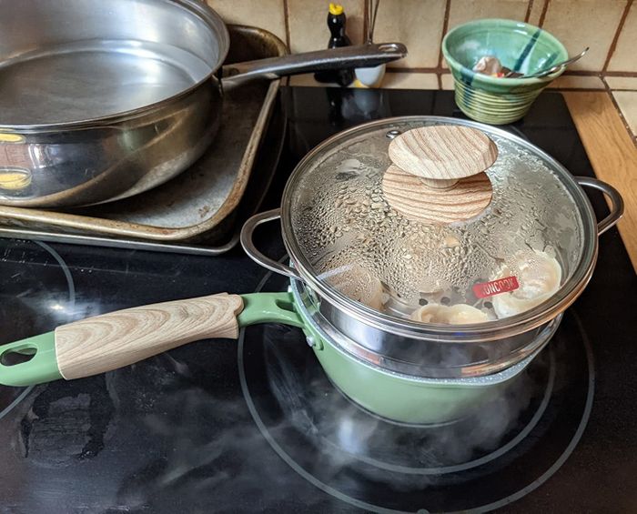 A reviewer demonstrates the green ceramic saucepan with elegant wooden accents on both the handle and lid.