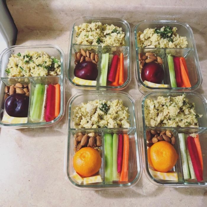A reviewer displays five containers, each filled with veggies, fruit, and chicken salad in their respective compartments.
