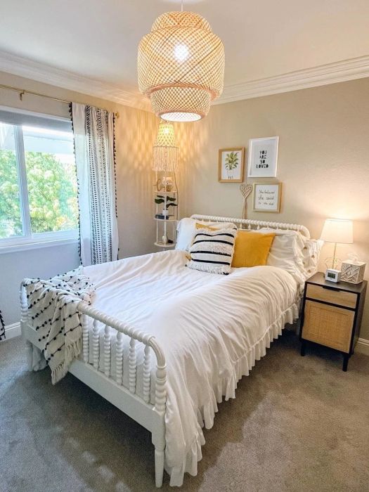 A cozy bedroom with a neatly made bed, decorative pillows, a side table with a lamp, framed artwork adorning the walls, and a charming wicker pendant light hanging overhead.