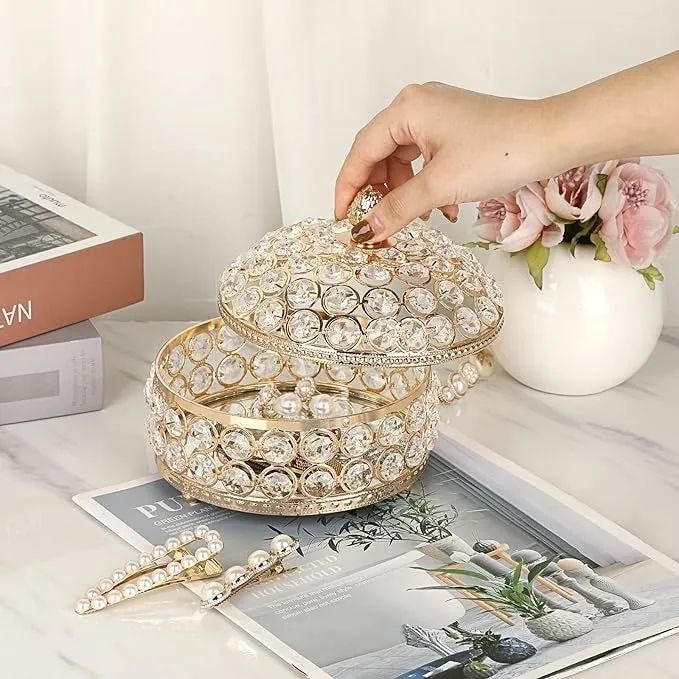 A model opens a sparkling round jewelry box on a marble table, surrounded by chic accessories