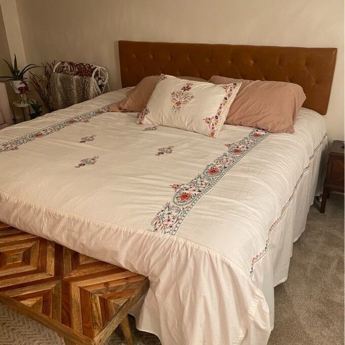 A stylish bedroom arrangement showcasing a large bed with an embroidered duvet and pillows, a tufted headboard, and a decorative bench placed at the foot of the bed