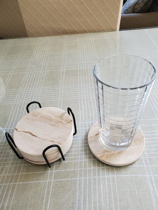 A reviewer displays five coasters stacked neatly in a metal holder, with one placed out with a glass on top.