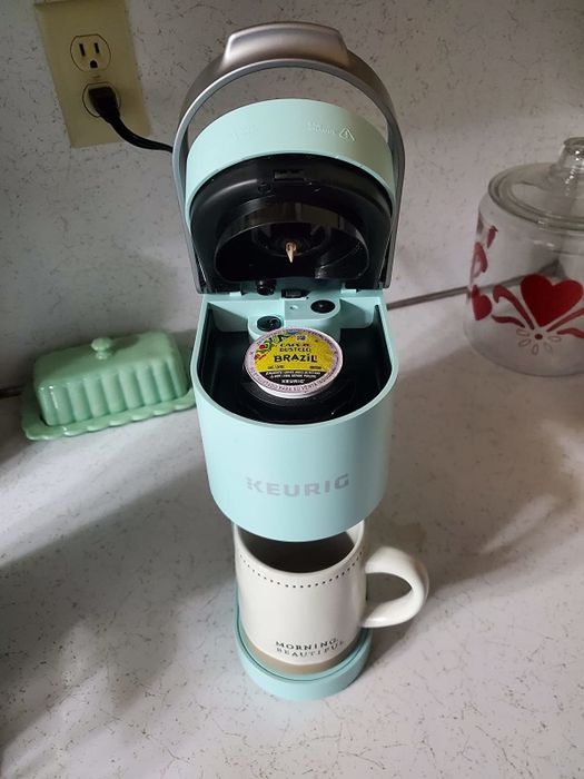 The same reviewer displays the open Keurig with a coffee pod ready inside.