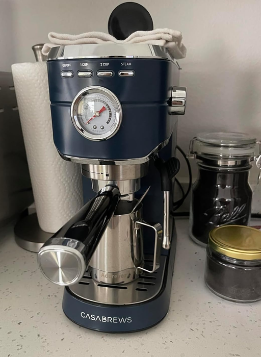 Espresso machine placed on a kitchen counter surrounded by jars and a roll of paper towels.