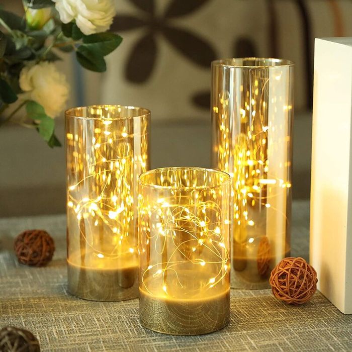 Three glass candle holders filled with string lights, arranged on a table to set a cozy, inviting atmosphere.