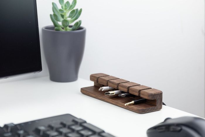 The dark wood cord organizer holds four different cords, arranged neatly on a clean white desk.