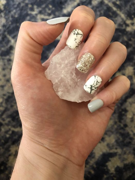 hand displaying various press-on nails featuring gray, marble prints, and glitter designs