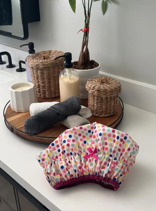 A bathroom counter with a potted plant, neatly arranged towels, and toiletries stored in wicker containers, featuring a cheerful, polka-dotted shower cap.