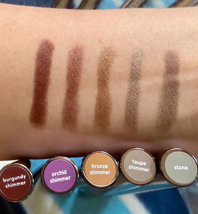 A swatch of five eyeshadow shades on a wrist, with labeled containers below showing the corresponding colors.