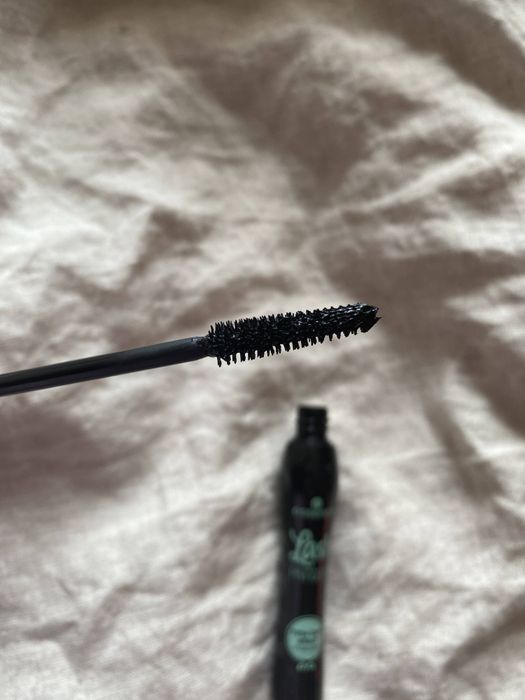 A close-up shot of a mascara wand with a partially open mascara tube in the background, emphasizing the bristle design.