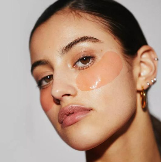 A model wearing under-eye gel patches and earrings, showcasing the rejuvenating effects of the product.