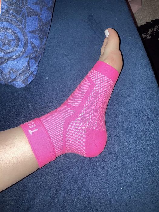 A foot wearing a pink, patterned compression sock while resting on a blue couch, highlighting comfort and support for a shopping article