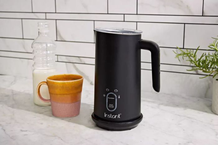 The Instant Pot Milk Frother resting on a marble countertop next to a coffee mug and a bottle of milk